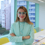 Smiling businesswomen in modern, colorful office with city views, exuding confidence and professionalism.