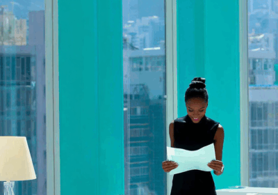 Women in a vibrant office setting, reading documents with city views through large windows.