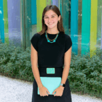 Women in stylish outfits holding colorful folders, standing outside modern, vibrant architectural buildings.